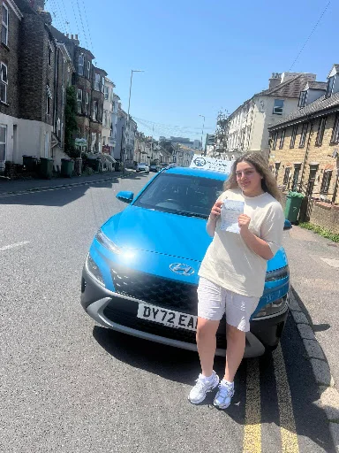 Lorri holding driving pass certificate beside tuition car